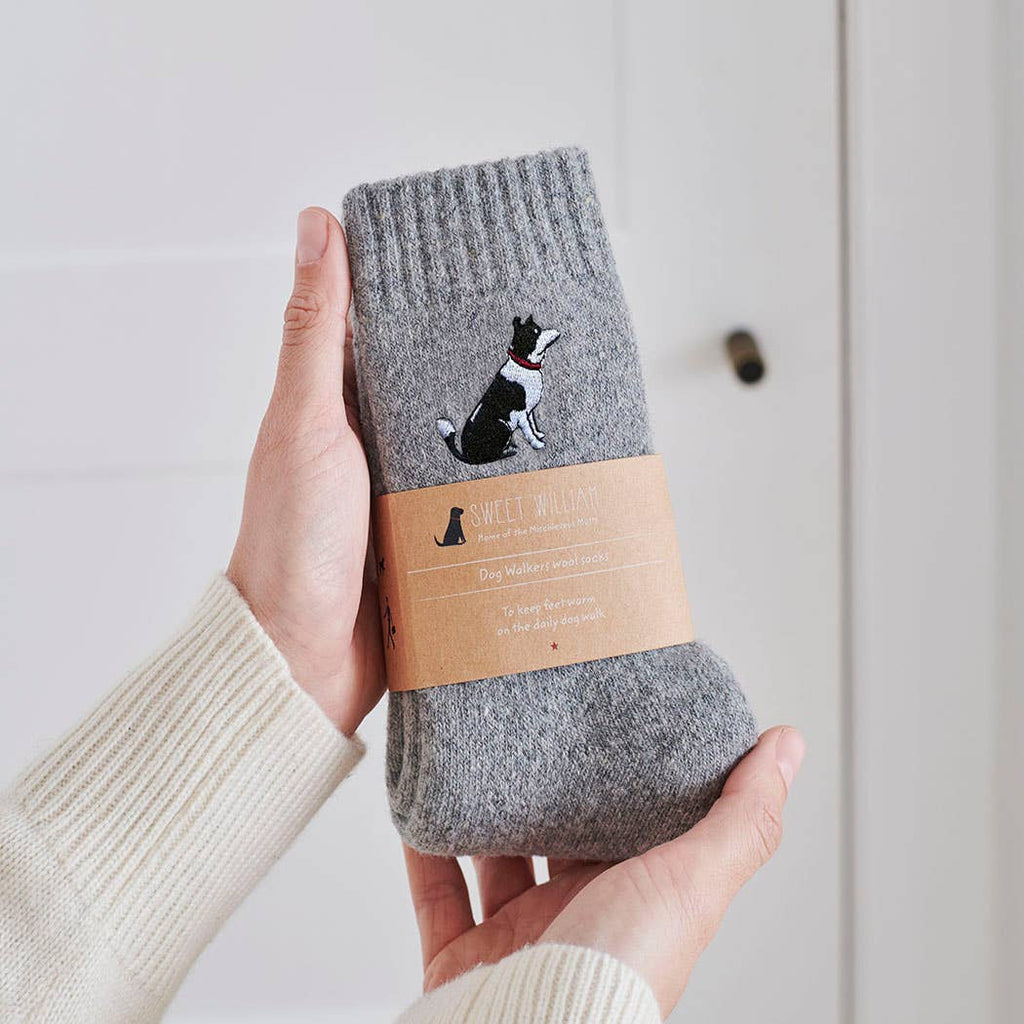 Gray woollen socks with a border collie illustration held by a person against a light background