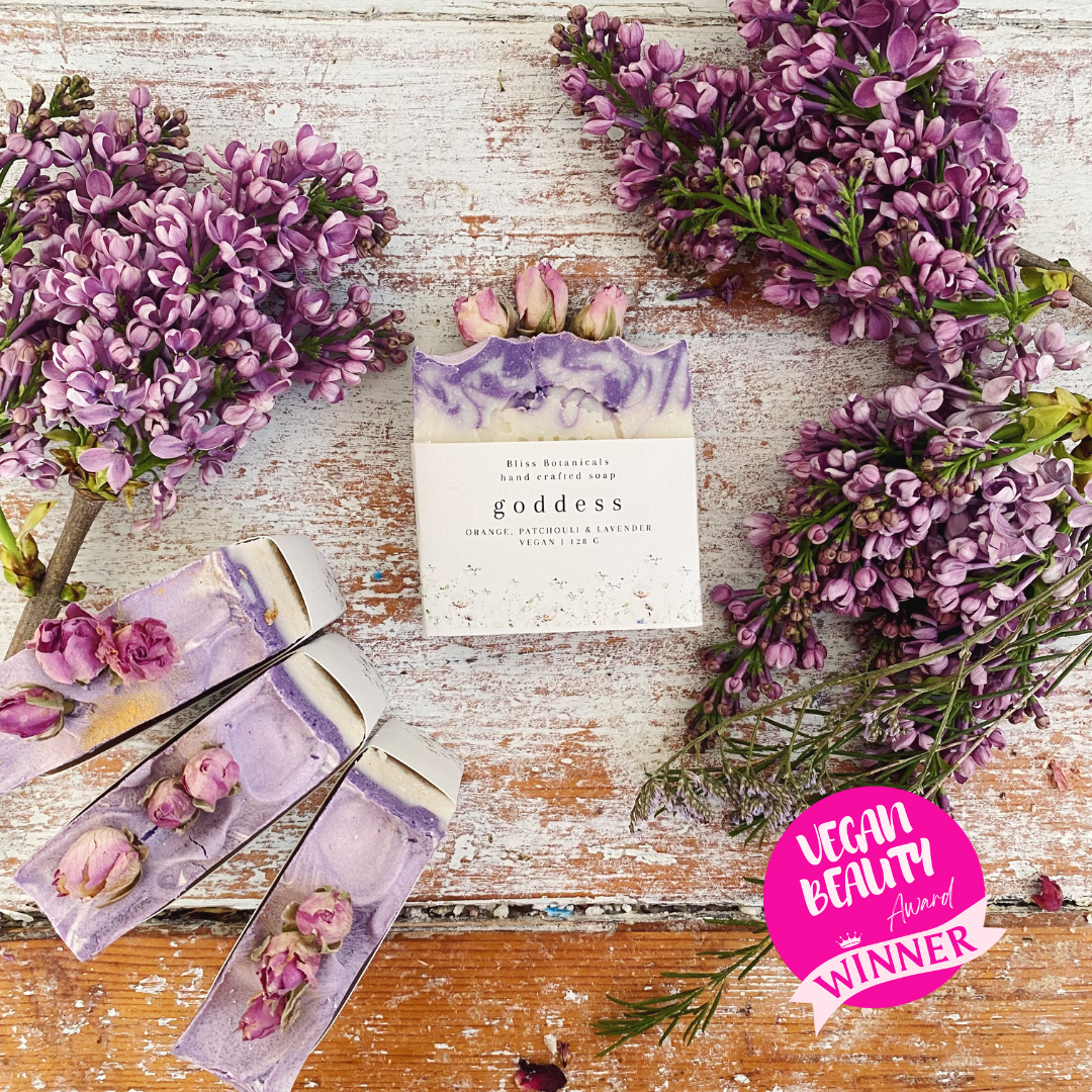 Bar of soap with packaging labeled 'goddess' surrounded by purple flowers on a wooden surface, with a 'Vegan Beauty Award Winner' badge.