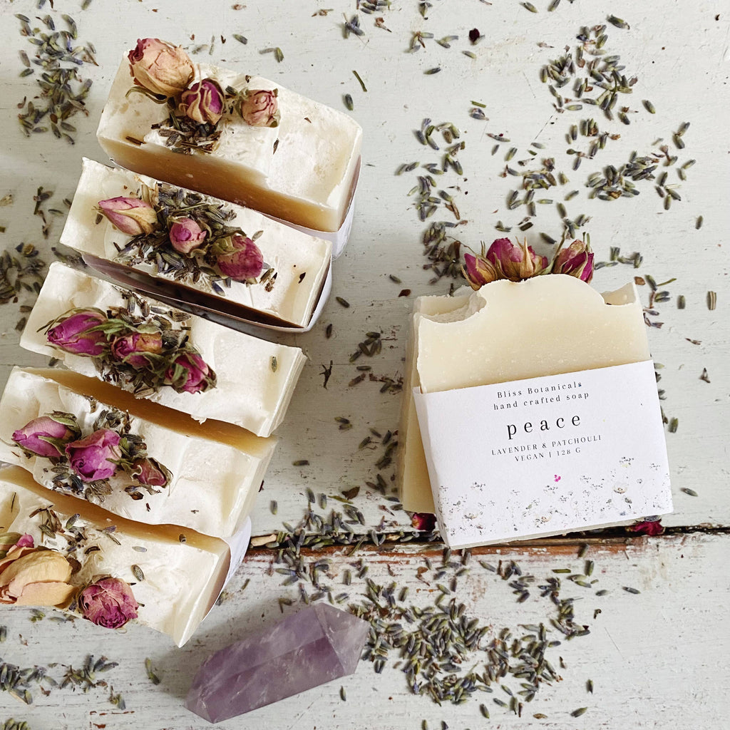 Handcrafted soap bars with dried flowers and a 'peace' label on a rustic surface with lavender.