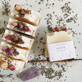 Handcrafted soap bars with dried flowers and a 'peace' label on a rustic surface with lavender.
