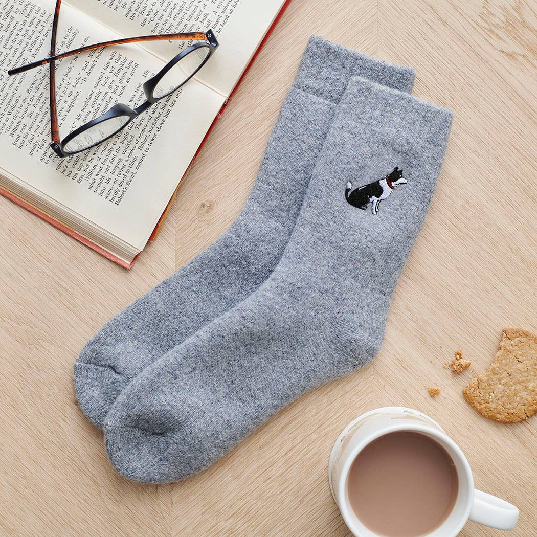 Gray socks with a border collie dog design on a wooden surface with a book, glasses, and a mug.